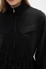 Campera negra de poliéster con cierre frontal, cuello alto, bolsillos con solapa en el pecho y cintura ajustable con cordón.