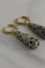 Aros colgantes con forma de gota, color crema con manchas negras, engarzados en aros dorados.
