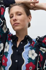 Camisa de manga larga, color azul marino, con estampado floral en tonos rojo, blanco y celeste. Presenta un diseño frontal con paneles ondulados en color celeste claro.