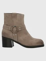 Bota corta de cuero color taupe, con caña de 14 cm, taco cuadrado de 6 cm y punta cuadrada. Presenta una correa con hebilla metálica alrededor del tobillo y cierre lateral.