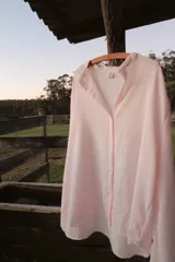 Camisa oversize color rosa claro a rayas verticales blancas, con cuello mao y mangas largas con puños elásticos.