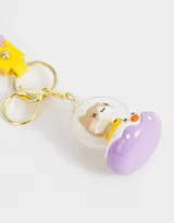 Llavero con dije de gatito dentro de una burbuja con base lila y correa de silicona lila con diseño de letras y dibujos en amarillo y blanco.