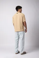 Camisa de manga corta color crudo, confeccionada en lino texturizado. Tiene cuello tipo cubano, cierre frontal con botones y corte recto.