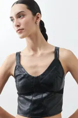 Top negro de eco cuero con corte crop, breteles finos y detalle de tul en el escote.