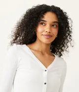 Cardigan blanco de punto con escote en V, manga larga y cierre frontal con botones negros.