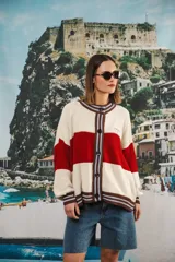 Cardigan tejido a rayas horizontales rojas y crema, con cuello redondo, cierre frontal con botones marrones y mangas largas abullonadas. Presenta ribetes a rayas en cuello, puños y ruedo. Tiene bordado el logo de la marca en el pecho.