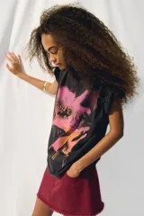 Remera negra de algodón con estampado del logo de la banda The Cure en tonos rosa y naranja. Corte oversized, cuello redondo y mangas cortas.