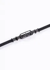 Pulsera de cuero negro con apliques de acero inoxidable plateado. En el centro presenta un dije rectangular con un águila grabada.