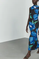 Vestido largo de tejido fluido con estampado floral azul sobre fondo negro. Tiene cuello subido con frunces y lazada, espalda descubierta, forro interior y abertura lateral en el bajo.