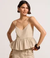 Blusa sin mangas color beige, con escote en V, breteles finos ajustables y peplum con volados en el bajo. Presenta lastex fruncido en la espalda.