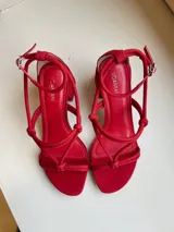 Sandalias rojas de cuero, con tiras finas con nudos en el empeine y pulsera con hebilla en el tobillo. Taco cuadrado de 7 cm.
