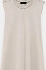 Vestido largo color beige, sin mangas, con cuello a la base y caída amplia. Confeccionado en tela estilo jogging.