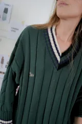 Buzo tejido verde con escote en V, cuello con rayas blancas y azul marino, y puños y ruedo con detalle de rayas.