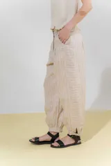 Pantalón de lino color marrón, con corte tipo barrel, tiro medio, pretina ancha con doble abotonadura, bolsillos laterales y pinzas en el frente. Ruedo con presilla permitiendo usarlo recto o fruncido al tobillo.