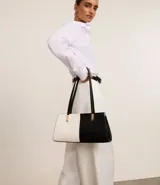 Cartera shoulder mediana de cuero sintético, con diseño bicolor blanco y negro y detalles metálicos dorados.