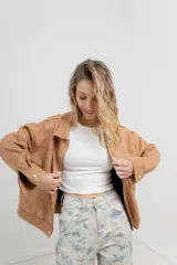 Chaqueta color camel, corte camisa de gamuza con elastano, corte recto abotonado en el frente con botones metálicos y bolsillos grandes en el frente.