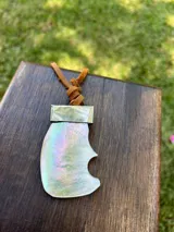 Collar con dije de nácar con forma irregular y detalles iridiscentes, engarzado en metal plateado y colgante de tiento de cuero marrón.
