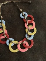 Collar con aros de acrílico entrelazados con tiento sintético color chocolate. Tiene nudo ajustable para regular el largo.