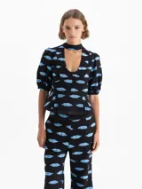 Top negro de jacquard con estampado de boquitas celestes. Presenta cuello con lazo, escote en V, mangas abullonadas con puños elásticos y un volado en el ruedo. Incluye recortes en el delantero y cierre trasero metálico.