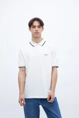 Chomba blanca de algodón con cuello clásico, media cartera de botones, bordado con la palabra 'Uniform' en el pecho y puños con rayas azul marino y rojo.