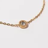 Pulsera dorada con cadena fina y dije circular con una circonita blanca engarzada.