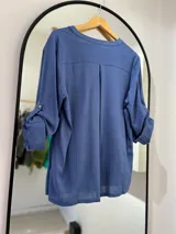 Blusa azul jeans de manga larga regulable, con escote en pico y botones en la parte delantera.