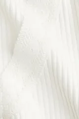 Top blanco de punto acanalado, corte ajustado y corto, con escote en V ribeteado en encaje y cierre frontal con tiras finas.