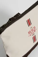 Neceser de lona color crudo con base y cierre superior en marrón oscuro. Estampado frontal con el texto "The Beach Club" en rojo y dos líneas verticales con franjas rojas y blancas.