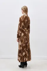 Vestido largo de viscosa estampada en tonos marrón y beige, con escote en V, mangas largas con puños elásticos y volado en el ruedo. Incluye lazo del mismo género para ajustar en la cintura.