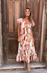 Vestido largo con estampado abstracto en tonos camel, naranja y blanco, con escote en V, mangas cortas con volados y falda con volados en el ruedo.