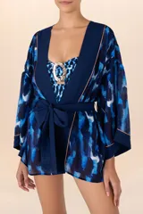 Kimono corto azul con estampado abstracto en tonos azules y blancos, con detalles dorados. Presenta mangas 3/4 amplias, cinturón liso y guarda frontal en color azul liso.