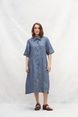 Vestido camisero midi de lino color celeste, con abotonadura frontal completa, manga corta ranglan, bolsillos laterales y volante en el ruedo.