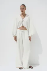 Pantalón blanco de lino, de corte ancho, tiro medio, con trabillas y cintura elástica ajustable con cordones.