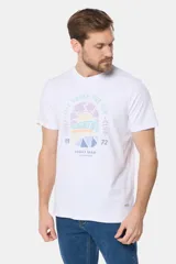 Remera blanca de manga corta con cuello redondo y un estampado gráfico frontal que simula un paisaje costero con un sol naciente o poniente, rodeado por texto circular que dice "SURF - LIFE UNDER THE SUN - CLUB".