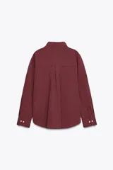 Camisa color borgoña a rayas verticales finas, de corte recto, con cuello solapa y manga larga. Tiene dos bolsillos de parche con solapa en el pecho y cierre frontal con botones.
