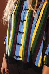 Cárdigan tejido con lurex, con cuello redondo, manga 3/4 y cierre frontal con botones forrados. Diseño con rayas verticales en tonos verde, azul y violeta sobre fondo negro con brillo.