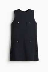 Vestido corto azul marino, de corte recto y sin mangas, con escote redondo y cierre oculto en la espalda. Tiene cuatro bolsillos de parche con botón dorado. Está forrado.