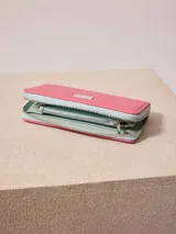 Billetera de poliuretano texturizado color rosado con cierre perimetral y logo metálico al frente.