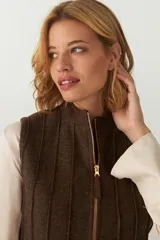 Chaleco color crema con cuello alto y cierre frontal con cremallera. Diseño con alforzas verticales en la parte superior delantera y trasera.