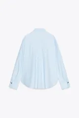 Camisa celeste a rayas verticales, de popelín, con cuello solapa, manga larga y cierre frontal con botones dorados.