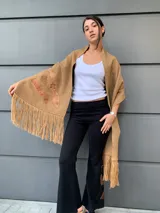 Chal tejido en lana color marrón claro con apliques de cuero y flecos en los bordes.