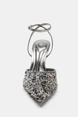 Zapato de tacón destalonado plateado con lentejuelas negras, tira al tobillo metalizada y punta fina.