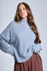 Sweater color crema de punto trenzado, con cuello alto y mangas largas.