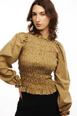 Blusa blanca de algodón con frunces tipo smock en el cuerpo, cuello redondo y mangas largas abullonadas con puños elásticos.