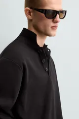 Polo de manga larga color negro, tejido en punto de algodón, corte relaxed fit, cuello solapa y cierre frontal con botonadura.