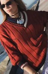 Buzo tejido verde con escote en V, cuello con rayas blancas y azul marino, y puños y ruedo con detalle de rayas.