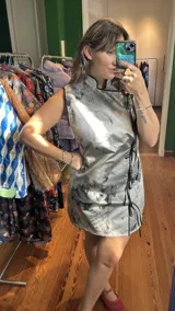 Vestido corto color verde lima con estampado floral blanco, corte cheongsam, cuello mao, sin mangas, con ribete negro y lazos decorativos en el lateral.