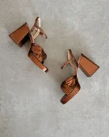 Sandalia de cuero vacuno color dorado, con plataforma y taco cuadrado. Presenta una tira delgada en el tobillo y detalle de nudo en la capellada.