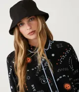Enterito corto negro con estampado de aliens y texto en blanco y naranja. Tiene cuello camisero, cierre frontal con botones y mangas largas con puños arremangados. Incluye riñonera negra.