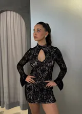 Vestido corto de encaje negro con forro color piel, cuello alto con abertura en el pecho y mangas largas acampanadas.
